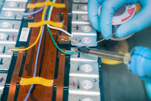 Technician use soldering iron to solder metal and wire of lithium-ion rechargeable battery. Repair module of Li-ion battery. Engineer hand holds soldering iron and tin-lead to solder electronic board.