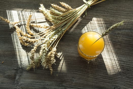 Freshly squeezed yellow juice and spikelets of ripe wheat on a wooden table in the sunlight.,,