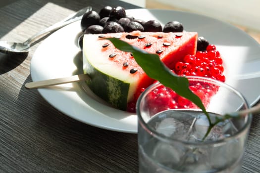 Summer snack. Fresh berries and fruits on a wooden table with green leaves of plants