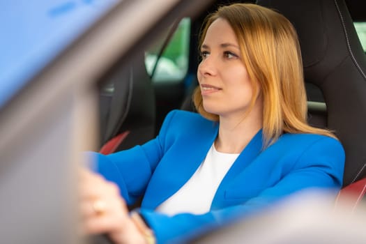 Smiling business woman driving a car in the blue suit