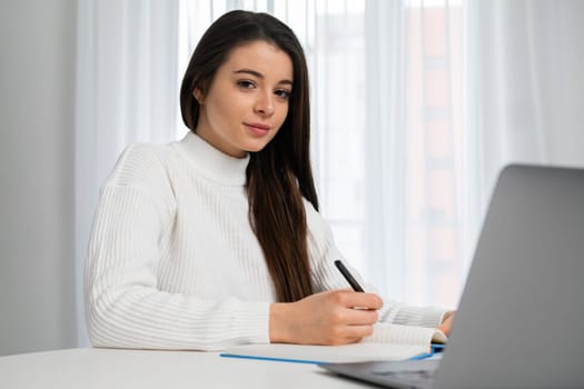 Portrait of an intelligent student wearing a white shirt, working on her laptop at home.