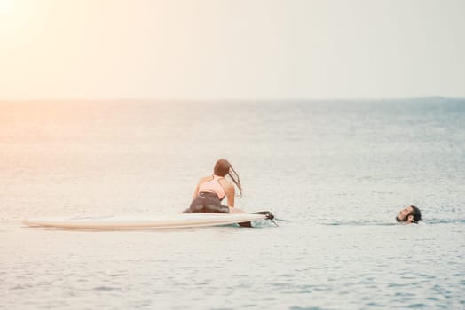 Sea woman and man on sup. Silhouette of happy young woman and man, surfing on SUP board, confident paddling through water surface. Idyllic sunset. Active lifestyle at sea or river