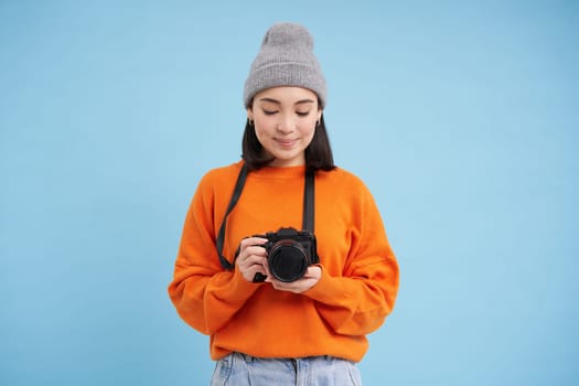 Passionate asian girl photographer, taking pictures on her digital camera, capturing moments outdoors, shooting photos, blue background.