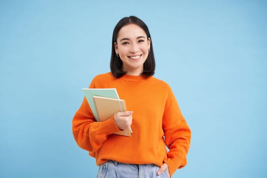 Education concept. Young smiling asian woman with notebooks, looking happy at camera, student going to uni.