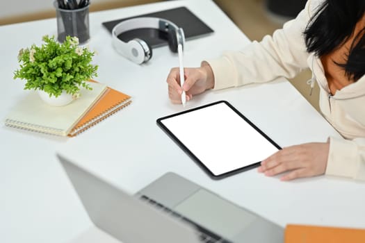 Close up view of young female freelancer working online, browsing internet via digital tablet at working desk.