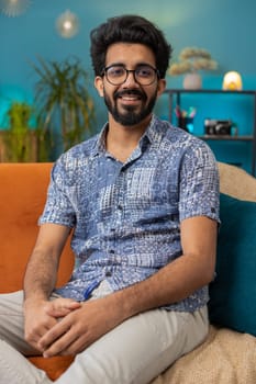 Portrait of happy calm indian man at home couch smiling friendly, glad expression looking away dreaming resting, relaxation feel satisfied concept good news, celebrate win. Hindu guy in living room