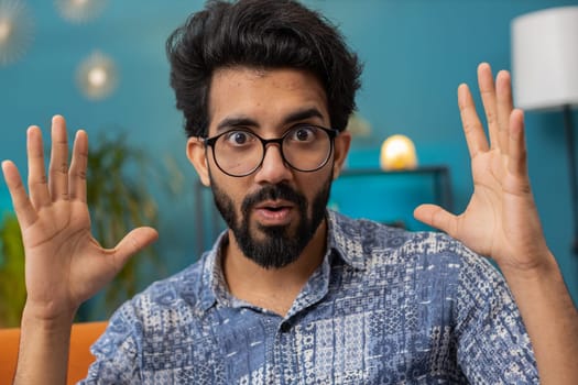 Oh my God, Wow. Young indian man surprised looking at camera with big eyes, shocked by sudden victory, good win news, celebrating. Portrait of excited amazed hindu guy at home apartment room on sofa
