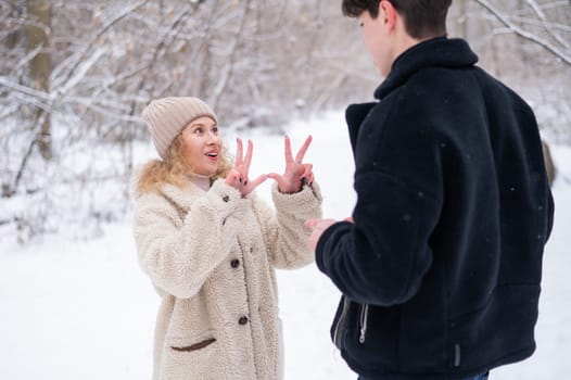 A young couple walks in the winter in the forest. Deaf Guy and a girl communicate using gestures outdoors