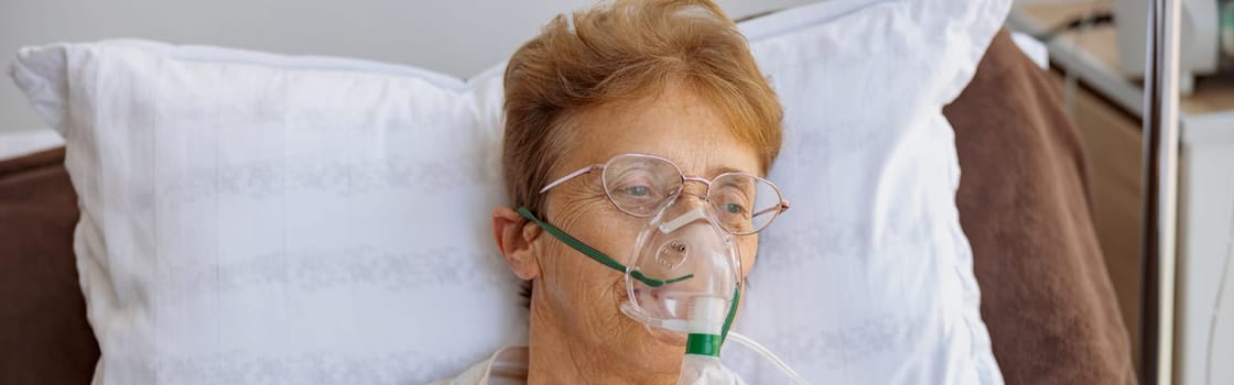 Senior patient in breathing mask lies in the ward during treatment for Covid-19. High quality photo