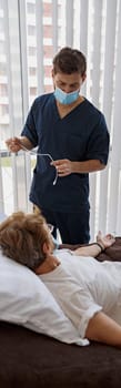 Doctor putting drip on arm of her patient in mask during pandemic of Covid 19. High quality photo