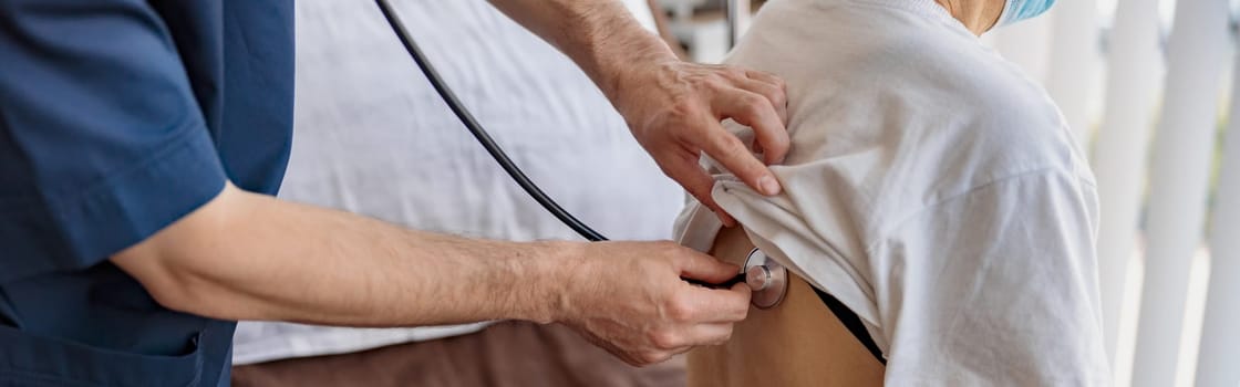 Close up of doctor listening to old woman's patient breathing, using stethoscope in hospital ward