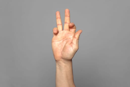 Strong hand of man making a funny gesture of peace and happiness isolated on gray background