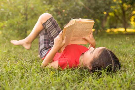 Adorable cute little girl reading book outside on grass.