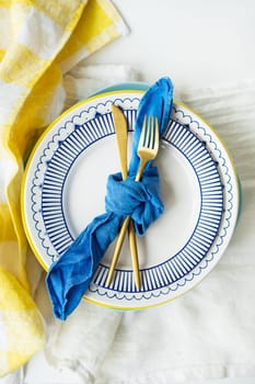 Gold cutlery is tied with a blue napkin, on which the plates are on a green-yellow linen napkin. Minimalist design, rustic. Birthday or wedding celebration. Serving design