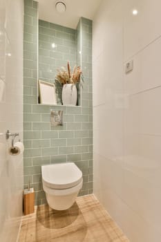 a white toilet in a small bathroom with green tiles on the walls and wood flooring around the toilet bowl