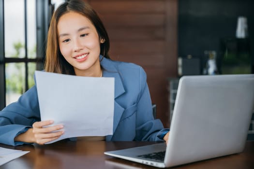 Asian smiling young business woman reading report document compare with laptop computer, Happy accounting female reviewing data in financial charts and graphs outside at cafe coffee shop