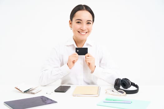 Happy businesswoman sits in office, shows credit card and smiles, pays contactless, waiting for payday, white background.