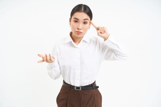 Corporate woman looks annoyed, points finger at head, mocks someone, scolding person, white background.