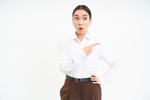 Portrait of korean woman, office lady pointing right, looking with curious face at banner, showing smth interesting, white background.