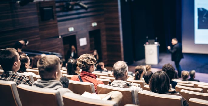 Speaker giving a talk in conference hall at business event. Rear view of unrecognizable people in audience at the conference hall. Business and entrepreneurship concept