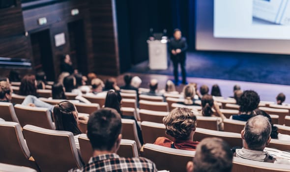 Speaker giving a talk in conference hall at business event. Rear view of unrecognizable people in audience at the conference hall. Business and entrepreneurship concept