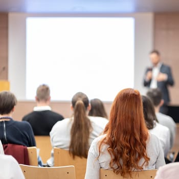 Speaker giving a talk in conference hall at business event. Rear view of unrecognizable people in audience at the conference hall. Business and entrepreneurship concept