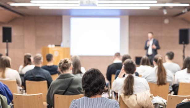 Speaker giving a talk in conference hall at business event. Rear view of unrecognizable people in audience at the conference hall. Business and entrepreneurship concept