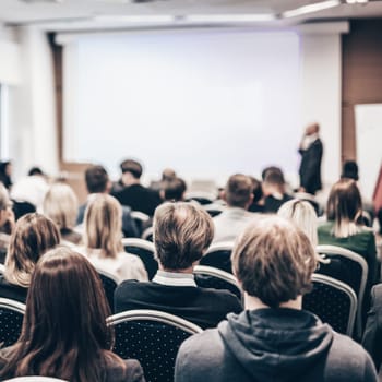 Speaker giving a talk in conference hall at business event. Rear view of unrecognizable people in audience at the conference hall. Business and entrepreneurship concept