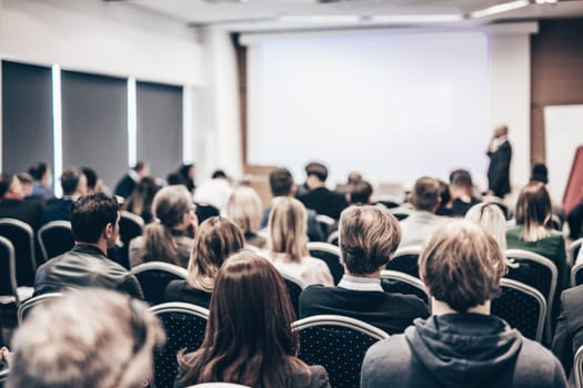 Speaker giving a talk in conference hall at business event. Rear view of unrecognizable people in audience at the conference hall. Business and entrepreneurship concept