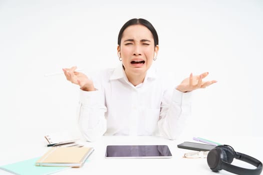 Sad japanese office manager, woman screaming and shouting, stressed out on work, sits in office with distressed emotions, white background.