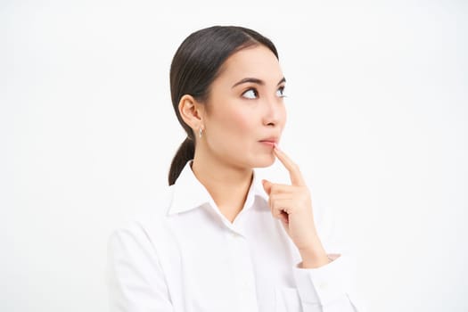 Portrait of businesswoman, asian lady boss thinks, looks thoughtful, pondering something with serious face, standing over white background.