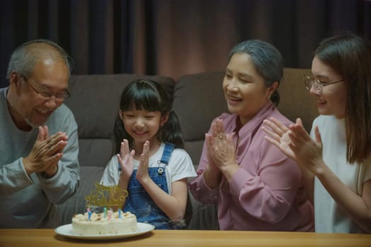 Birthday surprise. Happy Asian family grandparents and mother celebrating enjoy birthday party with cake of granddaughter at home in night time