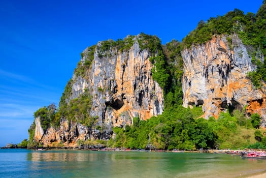 Long tail boats along cliff rocks near the beach, Tonsai Bay, Railay Beach, Ao Nang, Krabi, Thailand.