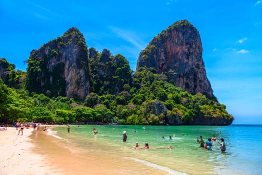 Rocks, water, tropical white sand beach and people swimming in emerald azure water of bay, Railay beach west, Ao Nang, Krabi, Thailand.