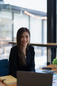 Portrait of a woman business owner showing a happy smiling face as he has successfully invested her business using computers and financial budget documents at work.