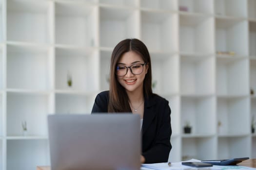 Portrait of a woman business owner showing a happy smiling face as he has successfully invested her business using computers and financial budget documents at work.