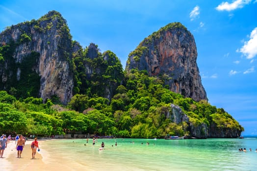 Rocks, water, tropical white sand beach and people swimming in emerald azure water of bay, Railay beach west, Ao Nang, Krabi, Thailand.