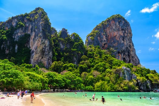 Rocks, water, tropical white sand beach and people swimming in emerald azure water of bay, Railay beach west, Ao Nang, Krabi, Thailand.