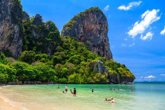 Rocks, water, tropical white sand beach and people swimming in emerald azure water of bay, Railay beach west, Ao Nang, Krabi, Thailand.