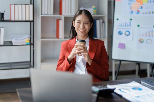 Portrait of a woman business owner showing a happy smiling face as he has successfully invested her business using computers and financial budget documents at work.