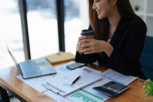 Portrait of a woman business owner showing a happy smiling face as he has successfully invested her business using computers and financial budget documents at work.