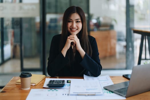 Portrait of a woman business owner showing a happy smiling face as he has successfully invested her business using computers and financial budget documents at work.