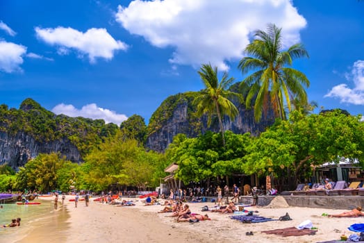 KRABI, THAILAND- MARCH 2018: People sunbathing among coconut palms on Railay beach west, Ao Nang, Krabi, Thailand.