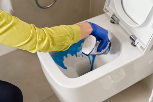 Wall mounted toilet cleaning with detergent. Woman hotel maid cleans a bathroom toilet with a scrub brush. household service. Modern flush toilet. Cleaning