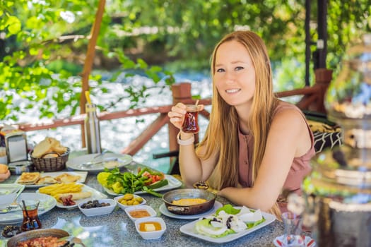 woman tourist eat Turkish breakfast. Turkish breakfast table. Pastries. Vegetables. Olives. Cheeses, fried eggs. Jams, tea in copper pot and tulip glasses. Wide composition.