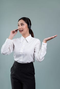Asian female call center operator with smile face advertises job opportunity, wearing a formal suit and headset holding hand gesture for product on customizable isolated background. Enthusiastic