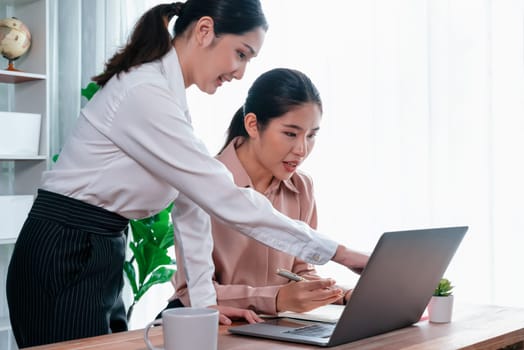 Two young office lady colleagues collaborating in modern office workspace, engaging in discussion and working together on laptop, showcasing their professionalism as modern office worker. Enthusiastic