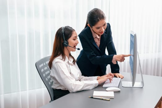 Asian female customer support operator wearing headset is guided by her supportive manager. Experienced colleague help operator handle a call with a client, providing advice and guidance. Enthusiastic