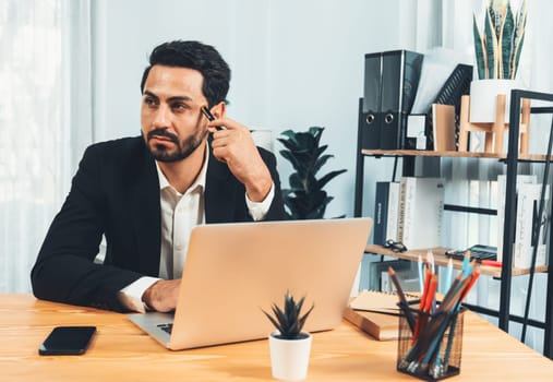 Modern professional businessman at modern office desk using laptop to work and write notes. Diligent office worker working on computer notebook in his office work space. fervent