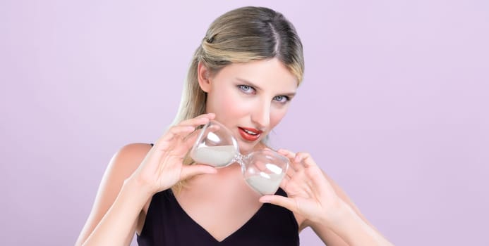 Alluring beauty model holding hourglass in forever young beauty concept of anti-aging skincare treatment for woman. Beautiful caucasian women portrait with perfect makeup in pink isolated background.